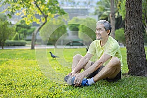 senior male in sportswear sitting under a tree,stretching legs in the city park