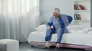 Senior male suffering sharp back pain, sick person getting up from bed, morning