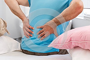 Senior male suffering sharp back pain, sick person getting up from bed, after rest