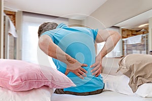 Senior male suffering sharp back pain, sick person getting up from bed, after rest