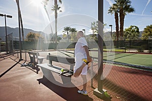 Senior male tennis player stretching leg on court