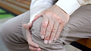 Senior male touching knee, sitting on bench, pain in joints, problems with knees photo