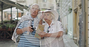 Senior male tourist asking woman for directions in town using a map in hands