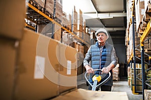 Senior male warehouse worker pulling a pallet truck.