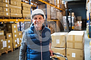 Senior male warehouse worker or a supervisor pulling a pallet truck with boxes.