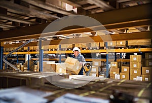 Senior male warehouse worker or a supervisor unloading a pallet truck with boxes.