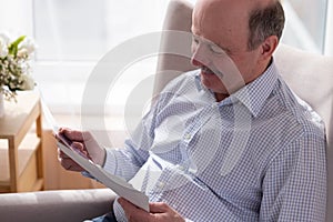 Senior man alone sitting on sofa at home holding photos thinking of memories