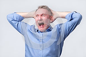 Senior man with angry grimace on his face,with mouth opened in shout