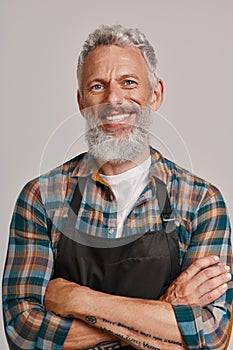 Senior man in apron smiling and looking at camera while standing against gray background