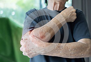 Senior man with arm pain. Old male massaging painful hand indoors. Old man hand holding his elbow suffering from elbow pain