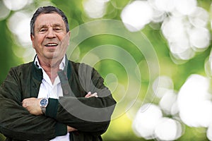 Senior man with arms crossed on defocused green nature background
