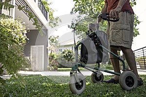 A senior man  as he strolls with his wheeling walker in garden