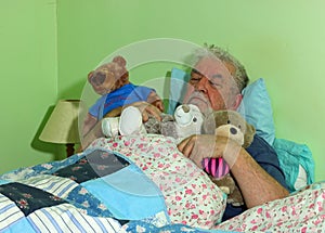 Senior man asleep in bed with soft cuddly toys.