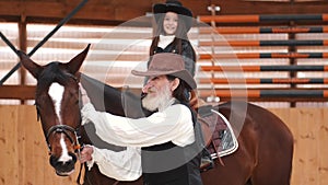 Senior man assisting granddaughter horseback riding in ranch