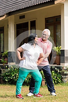 Senior man assisting his wife during warming up exercises outdoo