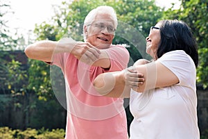 Senior man assisting his wife during warming up exercises outdoo