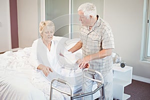 Senior man assisting ill woman in getting up from bed