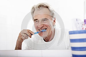 Senior Man In Bathroom Brushing Teeth