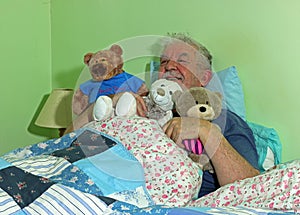 Senior man in bed with soft cuddly toys.