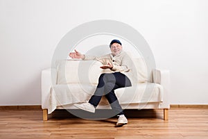 Senior man in beige sweater sitting on sofa, studio shot.