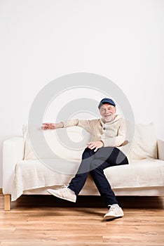 Senior man in beige sweater sitting on sofa, studio shot.