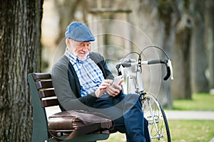 Senior man with bicycle in town, holding smart phone, texting