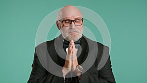 Senior man in black suit and bowtie making a plea with hands together