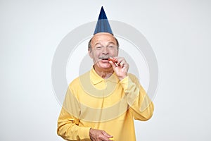 Senior man blowing party horn having excited look while celebrating birthday