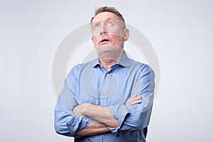 Senior man in blue shirt rolling his eyes up.