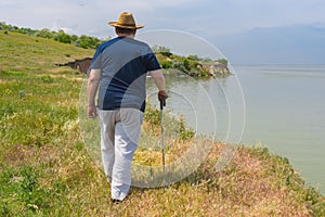 Senior man in blue t-shirt and light pants walking on abrupt riverside of the Dnepr River, Ukraine