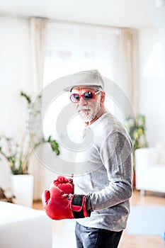 A senior man with boxing gloves having fun at home.