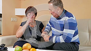 Senior man brings the tablet with a glass of water to his wife at home on the couch. Poor health of women. Taking care