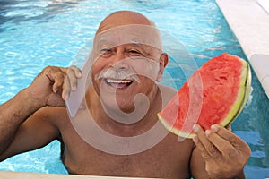 Senior man calling from swimming pool while eating watermelon