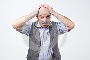 Senior man can not control panic and stress holding hands on head open mouth.