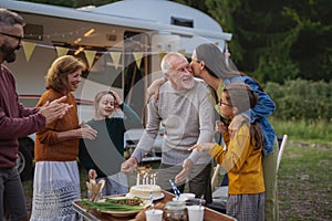 Senior man celebrating birthday outdoors at campsite, multi-generation family caravan holiday trip.