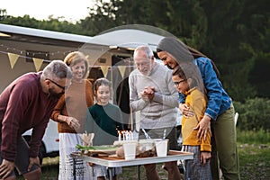 Senior man celebrating birthday outdoors at campsite, multi-generation family caravan holiday trip.