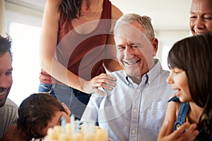 Senior man celebrating his birthday with family after blowing out candles on birthday cake, close up