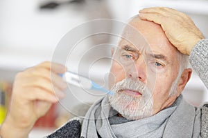 Senior man checking body temperature with thermometer