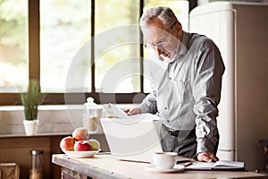 Senior man checking his papers in kitchen at home