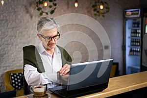 Senior man checking time while using laptop in a bar