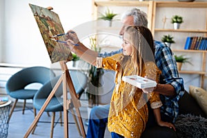 Senior man with child painting on canvas. Grandfather spending happy time with granddaughter.