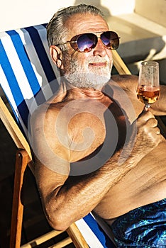 Senior man chilling and drinking wine on deck chair