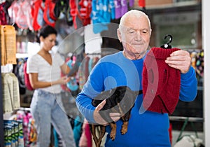 Senior man choosing winter clothes for his dog at pet shop