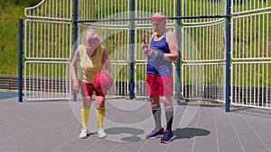 Senior man coach teaching grandmother with basketball dribbling exercise with ball on playground