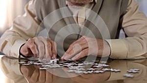 Senior man collecting puzzle, alzheimer disease awareness concentration exercise