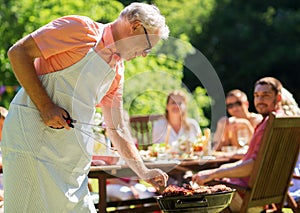 Senior man cooking meat on barbecue grill outdoors