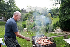 Senior man cooking pork barbecue on skewers