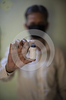 Senior man with corona preventive mask holding medicine ampul in his hand.