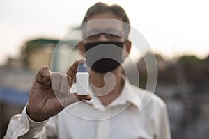 Senior man with corona preventive mask showing medicine ampul or vaccine standing on rooftop outdoor.