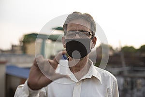 Senior man with corona preventive mask showing medicine ampul or vaccine standing on rooftop outdoor.